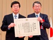 平口洋副大臣(左)からセコムに表彰状が授与された